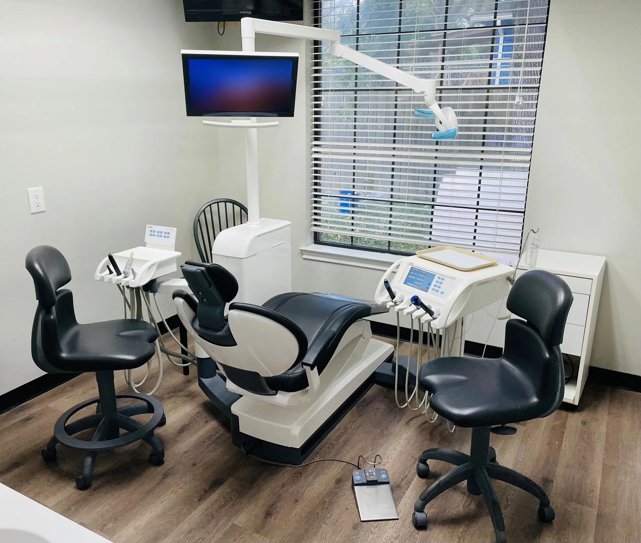 One of our treatment rooms: a dental chair, two stools, the instrument trays and a window with blinds